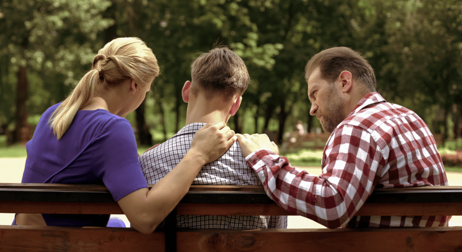 Mom and dad with their hands on sons shoulder sitting on a bench