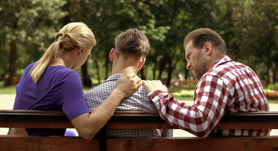 Mom and dad with their hands on sons shoulder sitting on a bench